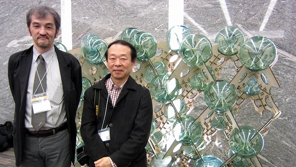 環境情報学部の小川克彦教授（右）と政策・メディア研究科の池田靖史教授。後方のオブジェは池田研究室の「ガラス玉ウォール」で、東日本大震災の被災地である気仙沼（宮城県）で浮きとして使われていた漁業用のガラス玉を1つ1つKinectで測定し、それぞれの形に合わせて木板を切り出した